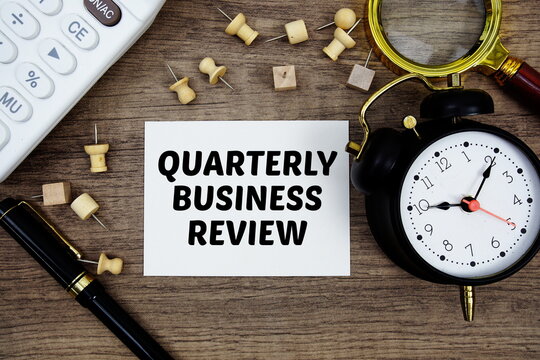 QBR Quarterly Business Review text written on notepad with pen, alarm clock, magnifying glass and calculator on wooden background