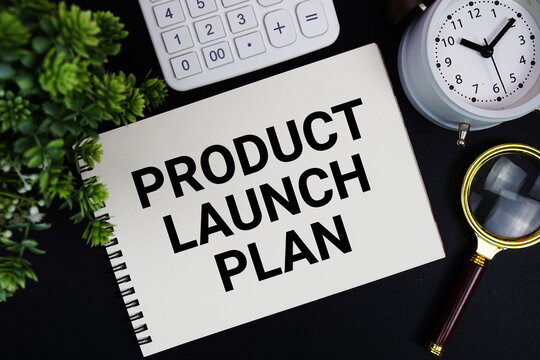 Product Launch Plan text written on notepad with alarm clock, magnifying glass and calculator on black background