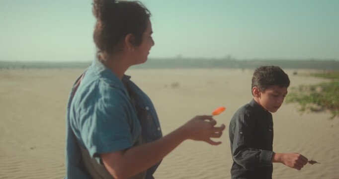 Two people walk together on a sandy landscape, enjoying popsicles in warm daylight