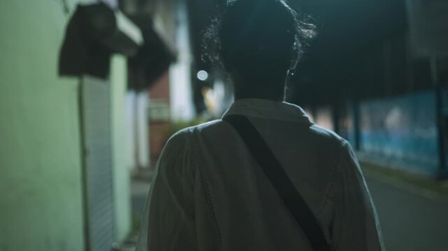 Person walks alone down a dimly lit street at night, passing closed storefronts
