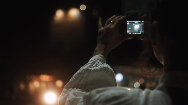 Young woman photographing illuminated city streets at night with a compact digital camera, capturing urban travel memories in a cinematic atmosphere
