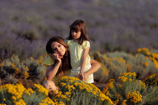 Tender Mother Holding Daughter Hand Against Cheek In Yellow Flower Field. Loving mom embraces her little girl closely in vibrant lavender field 