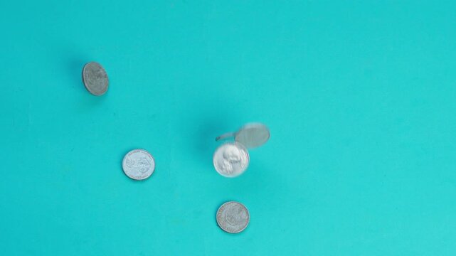 Silver coins fall, bounce, and scatter in slow motion across vibrant turquoise background