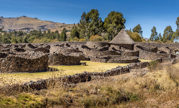Ancient circular stone structures at the archaeological site of Raqchi surrounded by Andean highland scenery under a clear blue sky