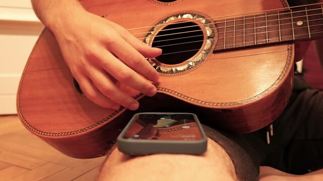 Musician playing acoustic guitar with metronome on phone