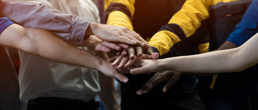 Foreman, engineer and workers standing putting their hands together in industry factory. Unity and teamwork concept