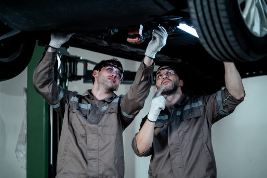 Professional Automotive Technician Carefully Inspecting Vehicle Suspension, Brake Components, and Wheel System Under a Hydraulic Car Lift During Routine Maintenance and Repair Service 