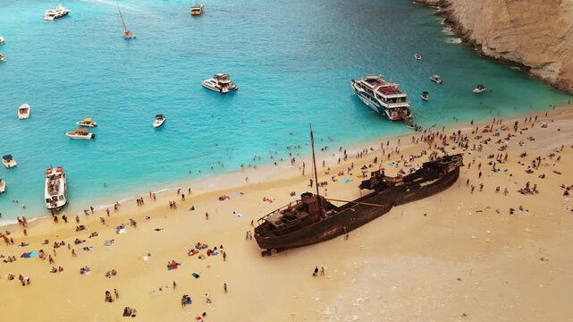 Aerial view of shipwreck beach with tourists swimming and boats docked in turquoise water.