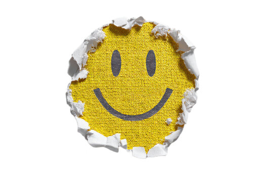Smiley face emoji revealed through torn white paper hole