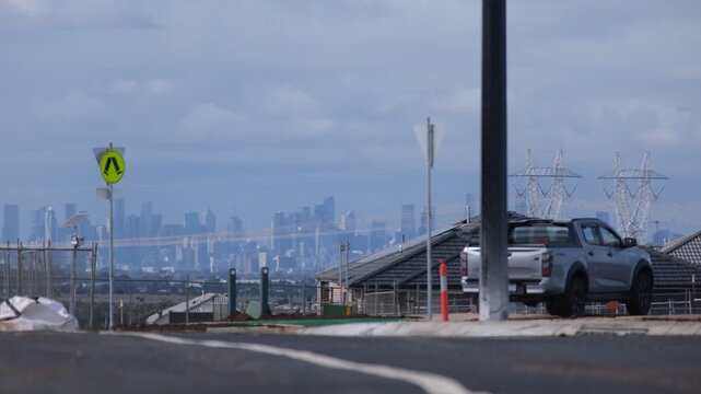 Hazy skyline of Melbourne CBD&nbsp;on the distant horizon, viewed from a suburban street under construction with high-voltage power pylons in Truganina, Melbourne, Australia.