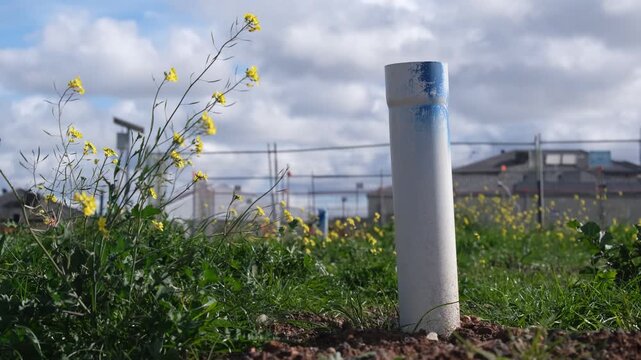 a white PVC utility pipe protruding from the ground on an undeveloped grassy lot in an outer suburb, Melbourne Australia, with construction fencing and house in background.