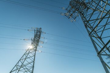 Highvoltage transmission towers stand against a clear sky with the sun shining brightly during the day