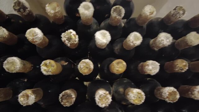 Stack of old wine bottles with dusty corks resting in cellar.