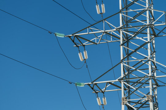 High voltage transmission tower with ceramic insulators and parallel power lines against clear blue sky, showing detailed lattice steel structure, utility grid infrastructure and outdoor engineering