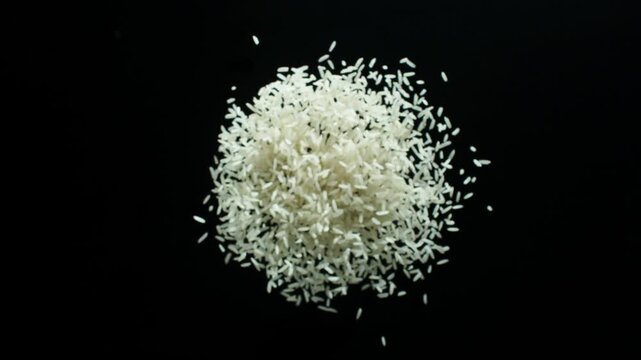 A compact sphere of uncooked white rice remains suspended before gradually expanding as individual grains separate across a dark background. Clean centered composition with controlled, gentle motion.
