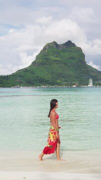 French Polynesia Vacation Travel woman walking on paradise motu beach on Bora Bora with Mount Otemanu wearing traditional pareo and Bikini in Tahiti. Raw vertical video of real woman without makeup