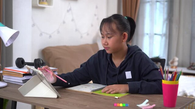 Young girl is diligently taking notes on important points from lesson during an online class at home
