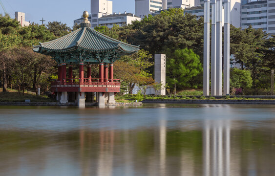 Traditional Korean pavilion by a serene lake with smooth water reflection and modern city background