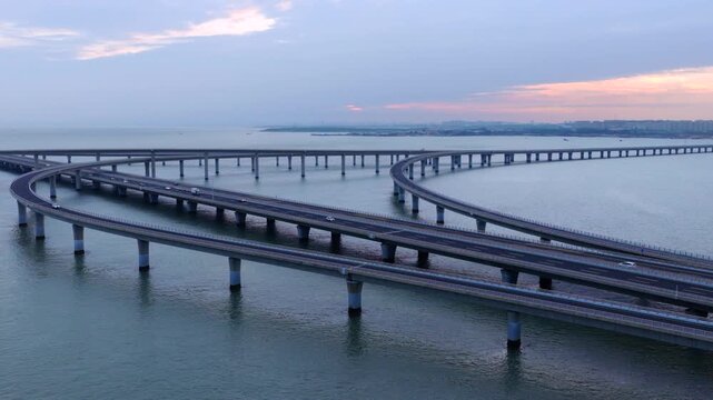 Aerial drone view of Qingdao Bay Cross-sea Bridge during blue hour dusk, heavy cargo trucks and vehicles driving on marine viaduct, grand Chinese transportation infrastructure