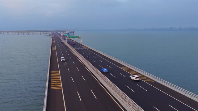 Blue hour aerial scenery of Jiaozhou Bay Bridge Qingdao, multi-level sea interchange highway, freight lorries with shipping containers traveling over sea, modern coastal transport engineering in China