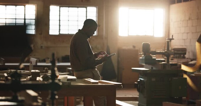 Carpenter, man and typing in workshop with tablet, research and check quote for furniture production. Creative, black person and woodworker in factory with tech, email and invoice for manufacturing.