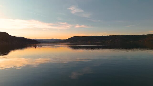 Spectacular wide aerial drone shot of two people on stand-up paddleboards on the calm, reflective waters of Salagou Lake (H&eacute;rault, France), while four Canadair firefighting aircraft golden hour sunset