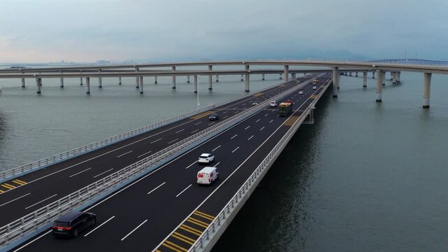 Aerial drone view of Qingdao Bay Cross-sea Bridge during blue hour dusk, heavy cargo trucks and vehicles driving on marine viaduct, grand Chinese transportation infrastructure