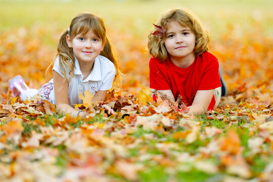 Autumn kids hold yellow leaves. Children play together in autumn park. Cute boy and girl lying on autumn grass. Children in autumn fall. brother and sister together. Happy kids friends face each other