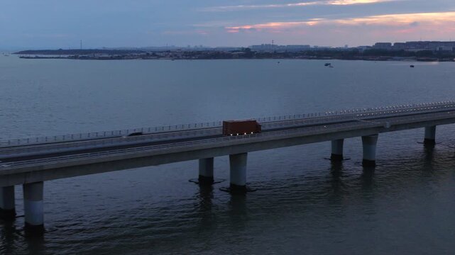 Evening twilight drone shot of Qingdao cross-sea highway, moving traffic and logistics trucks on giant bay bridge, landmark coastal infrastructure of Shandong China
