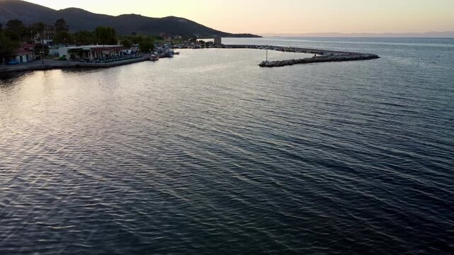 Drone footage of Thermi Port on Lesvos Island, Greece, featuring the historic stone windmill, fishing boats and tranquil Aegean coastline during a colorful summer sunset.