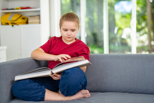 Child relaxing while reading a book at home. Happy kid exploring literature in home interior. Little reader enjoying bedtime story at home. Kid reading and learning in playroom.