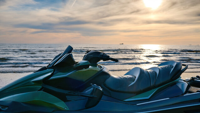 Modern jet ski parked on a sandy beach against the sea with bright sunset sky.