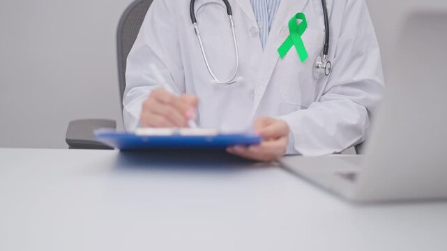 doctor using laptop and report notes on notebook. lime Green Ribbon for concept of May Celiac Awareness month, Lyme disease, September Lymphoma, Mental Health Awareness month and October Liver cancer