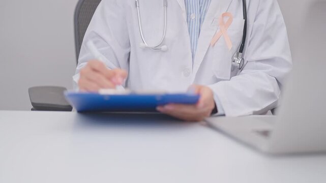 doctor using laptop and report notes on notebook. peach ribbon concept of September Uterine Cancer Awareness month, Endometrial, Gynecologic, Uterus and Ovaries, Endometriosis, June Vaginal cancer