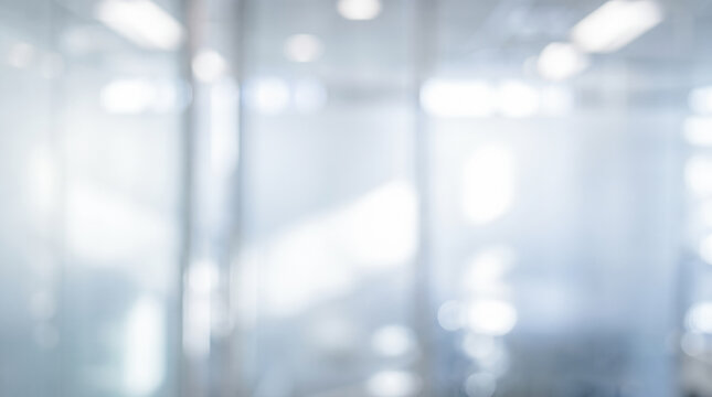 Blurred transparent glass office walls reflecting bright circular ceiling lights inside empty modern corporate business center hallway during quiet daytime working hours