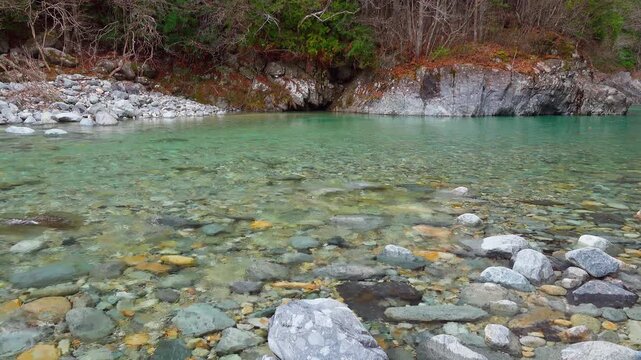 Autumn leaves dancing in the wind over the crystal clear emerald green water of Atera Valley Japan