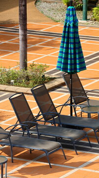 Closed striped patio umbrella beside empty pool loungers