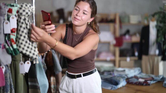While shopping, girl scans barcode on label of scarf, verifies authenticity of eco-friendliness of clothing production. Responsible consumption