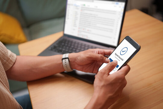 Man confirming a successful mobile payment on smartphone with laptop nearby, showing secure online transaction and digital authentication.