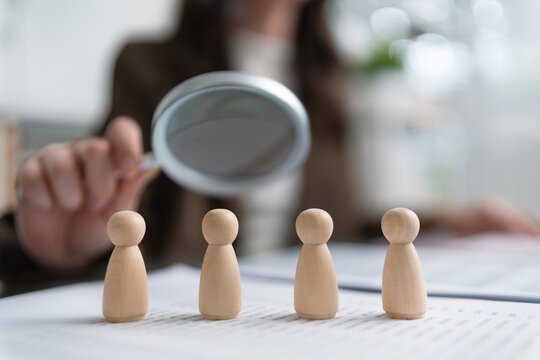 Magnifying glass over wooden figures symbolizes candidate screening and recruitment, highlighting human resources, hiring, workforce evaluation, and employee selection.