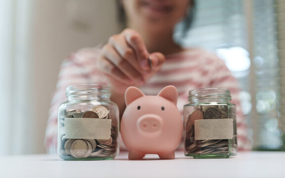 Asian Female placing a coin into a piggy bank beside savings and retirement jars, symbolizing disciplined investing and long-term financial security.