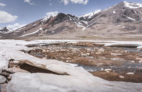 Landscape in the high Pamirs with rocky peaks and a river in a valley with melting snow. Panorama of rocky mountains on a sunny day and glaciers in a river valley