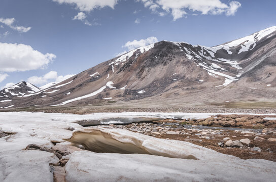 Landscape in the high Pamirs with rocky peaks and a river in a valley with melting snow. Panorama of rocky mountains on a sunny day and glaciers in a river valley
