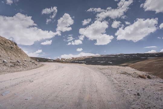 Dusty road of the Pamir Highway winds and twists in the valley of the Tien Shan mountains in Tajikistan in Pamir, landscape in the high desert mountains for background