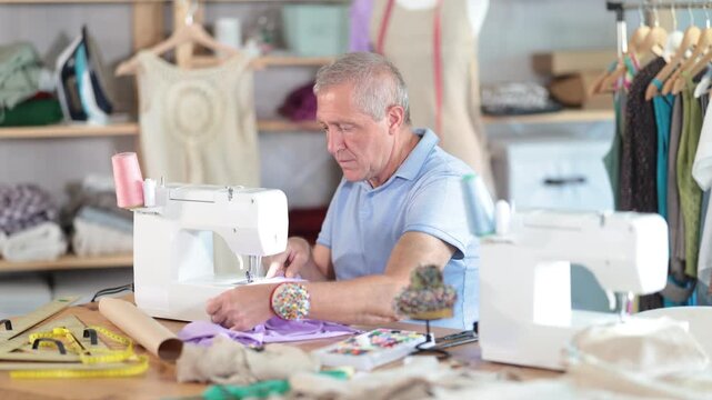 Mature man works as a tailor in a sewing workshop. Production of clothes according to individual measurements. Man sews a sample of clothes
