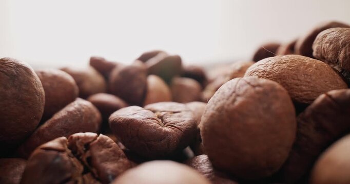 Macro tracking shot of roasted coffee beans shifting across tabletop surface with shallow depth of field and slow dolly motion.