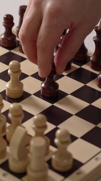 Hand carefully advances a dark pawn across the polished wooden board during an afternoon match of skill and intense focus while creating a classic master strategy in a quiet room
