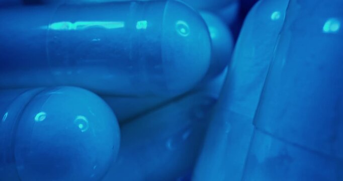 Slow motion close up of blue capsules sliding in medicine bottle on conveyor belt in production, macro probe lens.