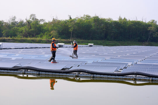 Workers are cleaning solar panels in a large body of water, a clean energy source for electricity generation.