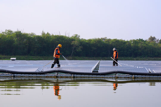 Workers are cleaning solar panels in a large body of water, a clean energy source for electricity generation.